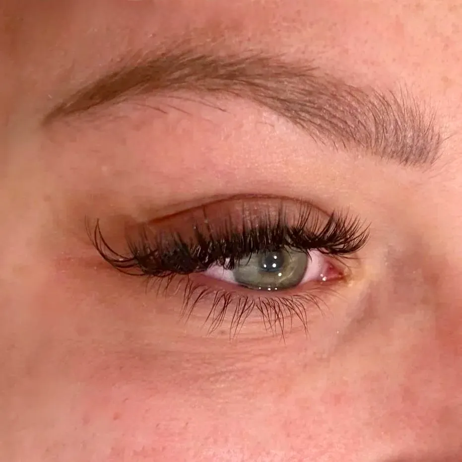 Finished lash extensions on an open green eye, wispy and textured along the lash line