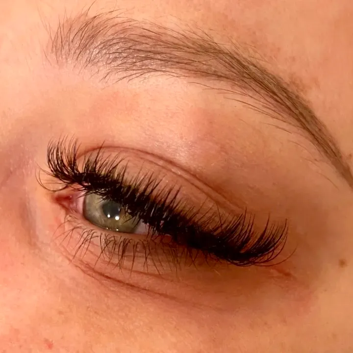 Volume lash extensions seen from the side on a closed eye, dense fans holding a soft upward curl