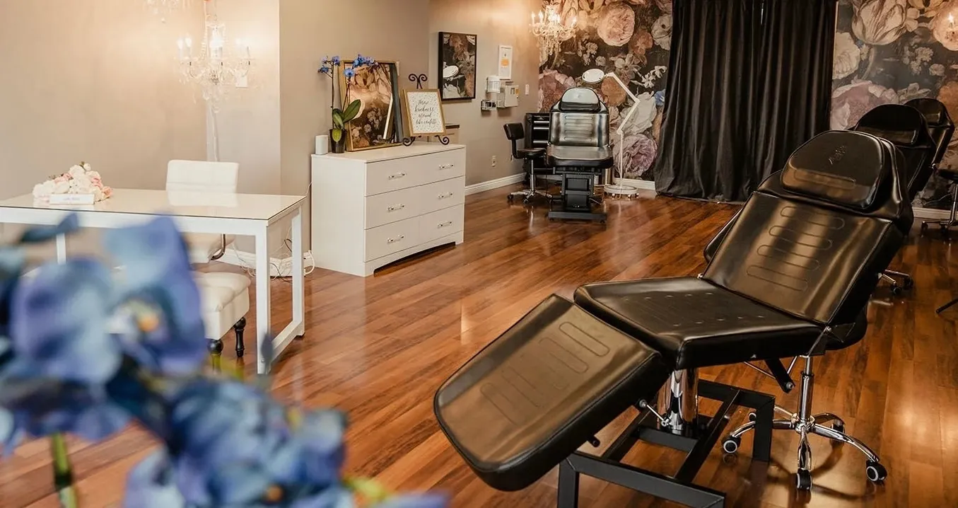 Black leather lash bed at Open Circle Salon facing the floral feature wall, with the reception desk and crystal chandeliers behind it