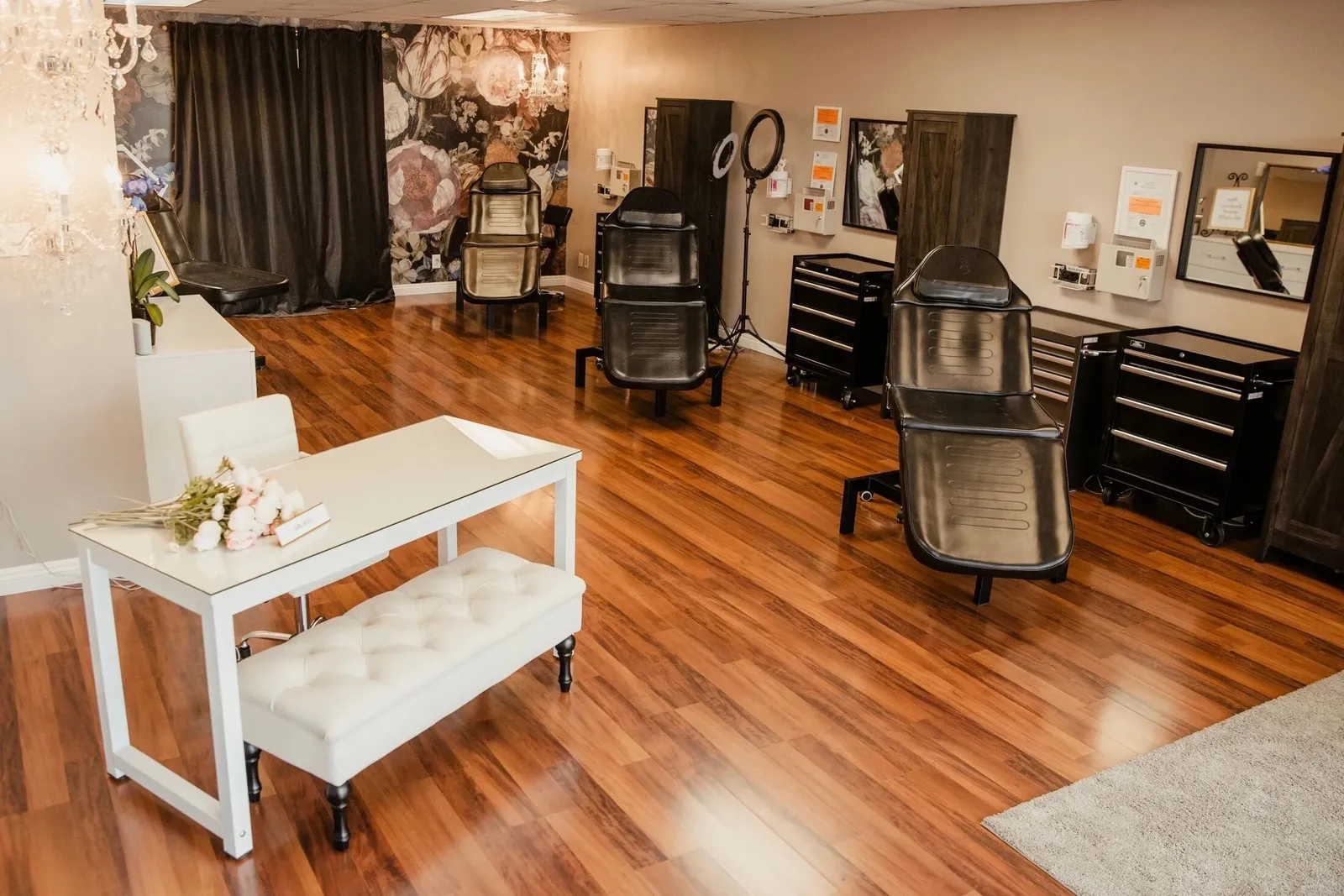 Wide view of the Open Circle Salon floor showing three lash and brow beds, rolling equipment carts, a ring light, and the white glass reception desk