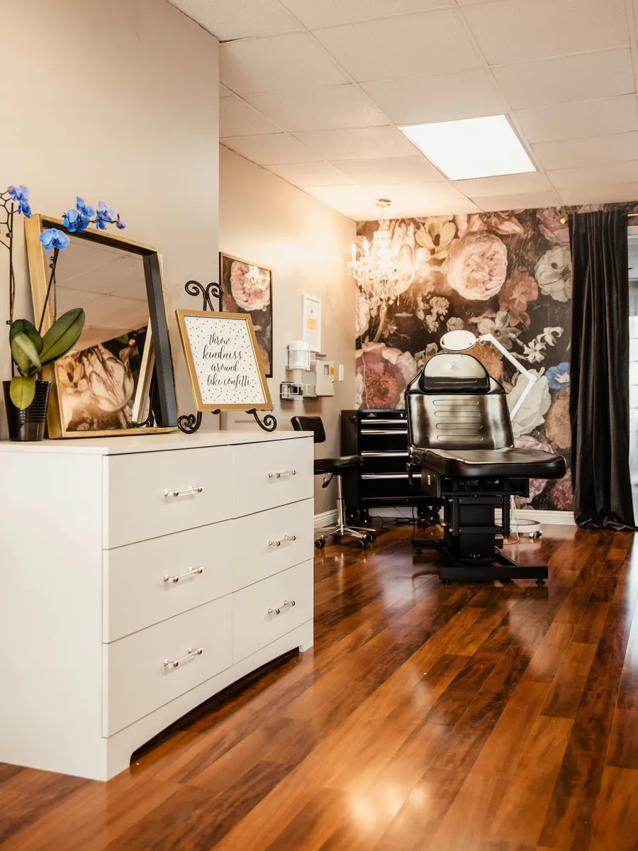 Treatment area at Open Circle Salon in Huntington Beach, with a reclining lash bed against a dark floral feature wall and a crystal chandelier overhead