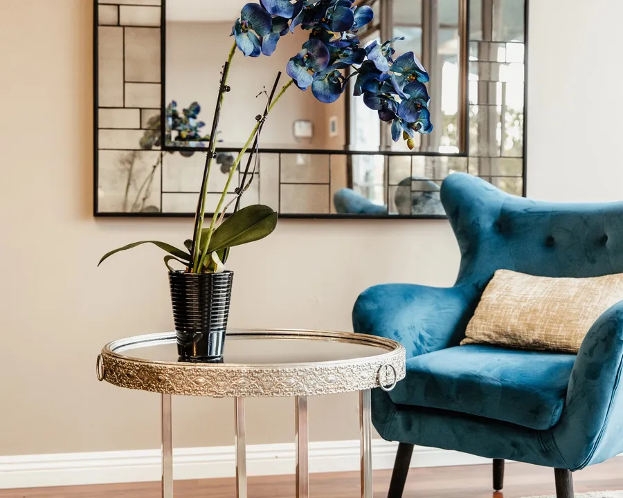Waiting area at Open Circle Salon with a teal velvet armchair, mirrored side table, and blue orchids